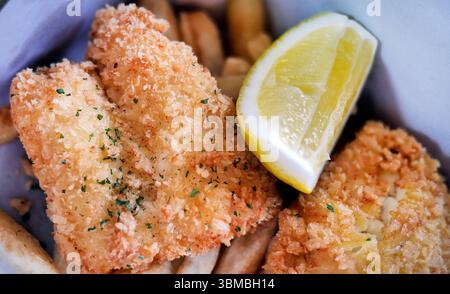 Specialità culinarie tradizionali inglesi o britanniche Fish and Chips, pesce fritto dorato con spicchi di limone in una scatola di carta da asporto per pranzo Foto Stock
