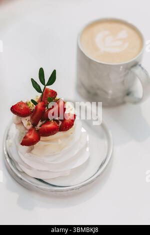 Mini pavlova di fragole con panna montata e pistacchi serviti accanto a un caffè di latte art in tazza di marmo Foto Stock