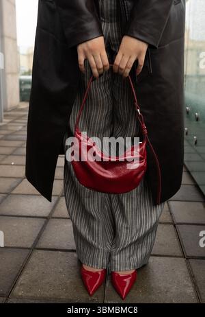 Dettaglio Street style: Donna in pelle nera con borsa baguette rossa e scarpe con tacco verniciato coordinato Foto Stock