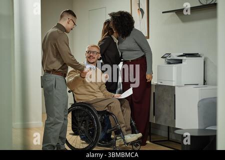 Uomo caucasico in sedia a rotelle che si impegna con un team multietnico Foto Stock