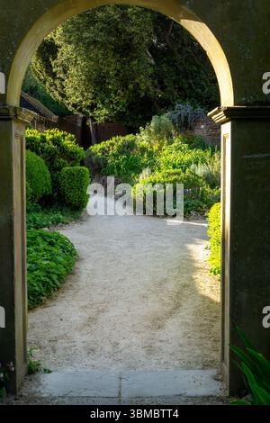 Un percorso attraverso i giardini Bridge End di Saffron Walden, Essex, incorniciato da un arco che conduce a un vivace giardino. Foto Stock