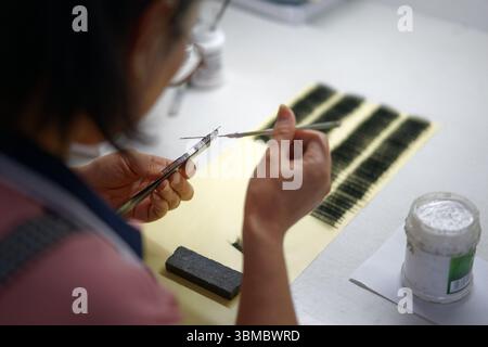(250626) -- QINGDAO, 26 giugno 2025 (Xinhua) -- Un lavoratore applica colla sulle ciglia in una falsa base di produzione di ciglia nella città di Pingdu, Qingdao, nella provincia di Shandong della Cina orientale, 25 giugno 2025. Lo sviluppo della falsa industria delle ciglia a Pingdu iniziò negli anni '1970 Oggi, oltre 5.000 aziende e circa 60.000 dipendenti sono coinvolti nel settore locale. Ogni anno, circa 120 milioni di paia di ciglia false prodotte a Pingdu vengono vendute all'estero, portando un valore di produzione annuo di circa 10 miliardi di yuan (circa 1,4 miliardi di dollari). Negli ultimi anni, con l'implementazione mirata Foto Stock