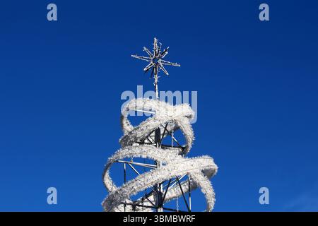 La scultura dell'albero di Natale con cornice metallica avvolta da spirali bianche della ghirlanda, sormontata da una stella, si erge su un cielo azzurro vivace, che mette in risalto le festività Foto Stock