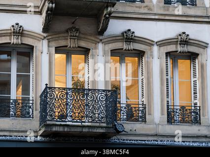 Un balcone decorativo in ferro battuto fronteggia alte e ampie finestre ad arco che si illuminano calorosamente dalle luci interne dietro facciate ornate in pietra su una strada parigina Foto Stock