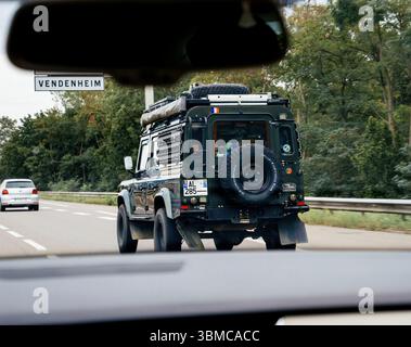 Boulogne, Francia - 24 agosto 2023: Una Land Rover Defender dotata di attrezzatura per il tetto sta viaggiando sull'autostrada vicino a Vendenheim, seguita dalla fot Foto Stock