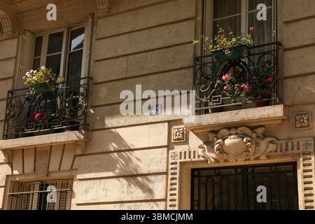 Una fotografia che mostra i dettagli architettonici di un condominio parigino. Due balconi adornati con piante in fiore e lavorati in modo intricato Foto Stock