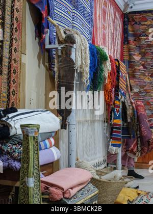 Marocco, Merzouga, 04 luglio 2025. Interno di un tradizionale laboratorio di tappeti berberi nella regione del Sahara, decorato con colorati tappeti e weav fatti a mano Foto Stock
