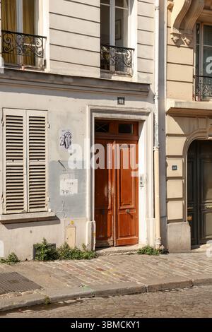 Un'affascinante fotografia che mostra una porta di legno marrone intemprata situata all'interno di un classico edificio parigino. La strada acciottolata di fronte aggiunge un tocco in più Foto Stock