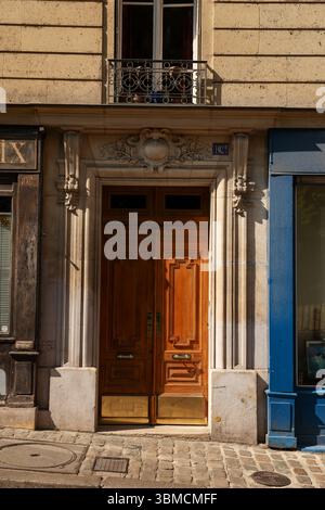 Una fotografia di un classico edificio parigino caratterizzato da una doppia porta in legno marrone ornata accentuata da ottone. La facciata dell'edificio è in pietra beige Foto Stock