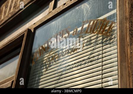 Foto ravvicinata di una finestra in legno intemprata che mostra un cartello vintage del negozio. La scritta dorata, leggermente sbiadita, legge VENTURES a l'HUILE Gourmandes." Foto Stock