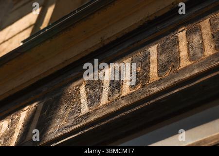 Uno scatto dettagliato in primo piano cattura un cartello esterno dell'edificio, parzialmente illuminato dalla luce del sole. Le lettere sbiadite suggeriscono un busi dimenticato Foto Stock