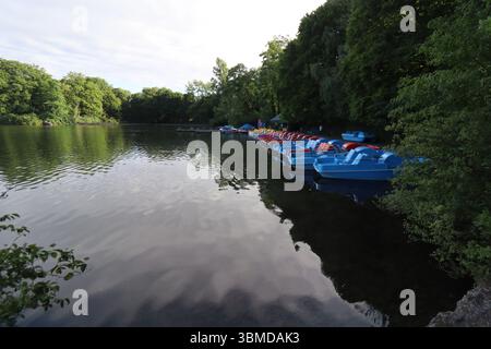 MONACO DI BAVIERA, GERMANIA - 24 GIUGNO 2025: Pedalò attraccate su un fiume calmo circondato da lussureggianti alberi verdi che si riflettono nell'acqua Foto Stock