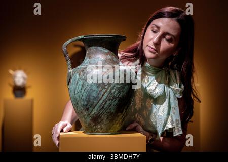 Londra, Regno Unito. 26 giugno 2025. Membro della galleria con «Una grande brocca romana di bronzo», circa i-IV secolo d.C., presso lo stand della Kallos Gallery all'apertura della Treasure House Fair presso il Royal Hospital Chelsea. La fiera presenta arte, antiquariato e design di settanta dei migliori commercianti britannici e internazionali ed è aperta al pubblico dal 26 giugno al 1° luglio 2025. Crediti: Stephen Chung / Alamy Live News Foto Stock