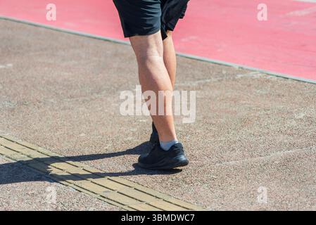 Parte inferiore di una persona non identificata che cammina su un marciapiede della strada durante la forte luce del sole. Attività, direzione, percorso. Foto Stock