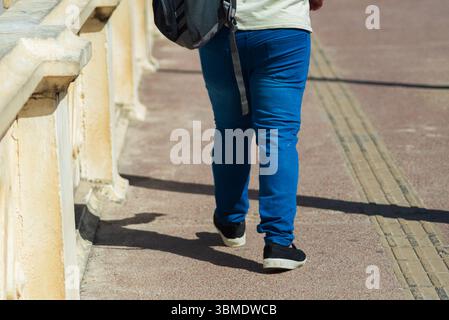 Parte inferiore di una persona non identificata che cammina su un marciapiede della strada durante la forte luce del sole. Attività, direzione, percorso. Foto Stock