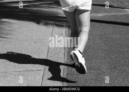 Parte inferiore di una persona non identificata che corre su un marciapiede della strada durante la forte luce del sole. Attività, direzione, percorso. Foto Stock