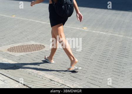 Parte inferiore di una persona non identificata che cammina su un marciapiede della strada durante la forte luce del sole. Attività, direzione, percorso. Foto Stock