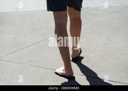 Parte inferiore di una persona non identificata che cammina su un marciapiede della strada durante la forte luce del sole. Attività, direzione, percorso. Foto Stock