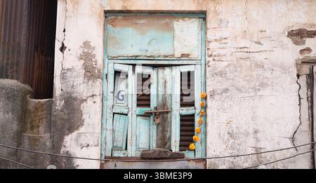 Vecchia casa a Mumbai, India, facciata rustica invecchiata con finestra di colore blu rotto, edificio con mattoni e pietra Foto Stock