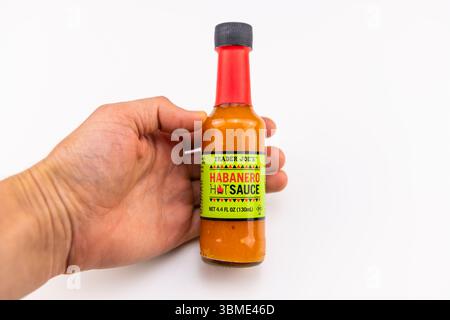 Napoli, Stati Uniti - 25 aprile 2022: Salsa calda Habanero della bottiglia di cibo rosso piccante di Trader Joe isolata su sfondo bianco, con la mano che tiene il primo piano Foto Stock