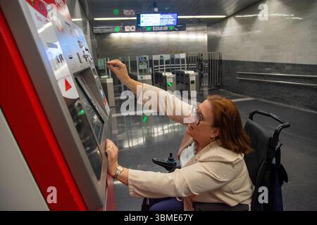 Donna in sedia a rotelle che convalida il biglietto alla macchina della stazione della metropolitana. Concetto di inclusione, trasporto pubblico adattato Foto Stock