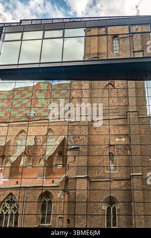 Riflesso di una chiesa storica con un tetto dai motivi vivaci su una moderna facciata in vetro, che mostra contrasti architettonici Foto Stock