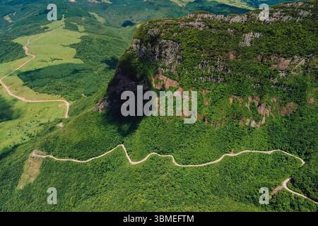 Tortuosa strada di montagna attraverso la lussureggiante foresta verde con scogliere spettacolari e viste panoramiche dal drone Foto Stock