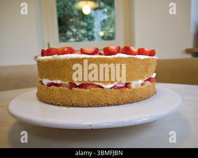Vista frontale della torta di fragole a strati con panna montata e fragole tagliate a metà, ripiena e ricoperta di frutta. Foto Stock