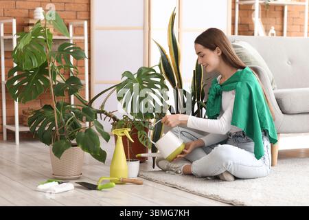 Giovane donna che innaffia la pianta di casa di Monstera a casa Foto Stock