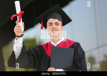 Studente laureato con diploma e libro vicino all'università Foto Stock