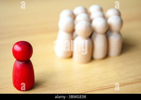 Figure in legno che si affacciano Su Un singolo peg beige in Un semicerchio su un tavolo in legno. Foto Stock