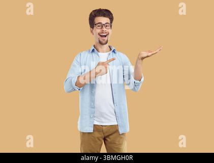 Ridendo felice uomo barbuto che punta il dito indice e mano sullo spazio di copia su sfondo beige. Foto Stock