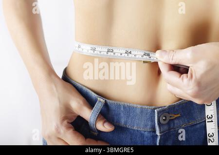 Modella caucasica in jeans blu con metro a nastro che mostra il suo stomaco piatto. Stile di vita sano e concetto di perdita di peso Foto Stock