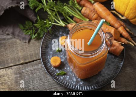 Succo misto naturale fresco, concetto di cibo sano. Vaso in vetro di succo di carota fresco con carote fresche e zucca su un tavolo rustico in legno. Copia spazio Foto Stock