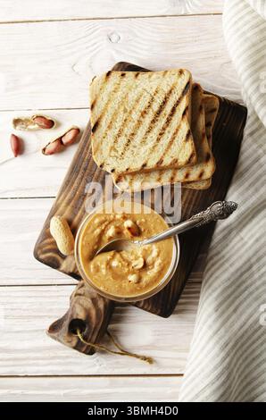 Distendere la vista sul recipiente di vetro con burro di arachidi sul tagliere con i toast a parte. Concetto di alimentazione sana Foto Stock