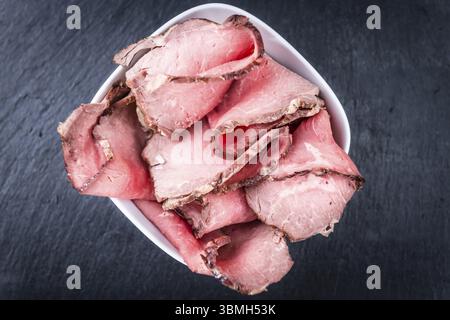 Porzione di roastbeef (tagliata a fette, focalizzata in modo selettivo) su una lastra di ardesia Foto Stock