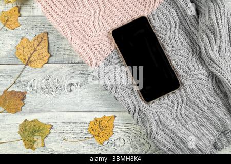 Foglie autunnali gialle, una tazza di tè e uno smartphone su un vecchio sfondo di legno con spazio vuoto per il testo. la vista dall'alto. posizione piatta Foto Stock
