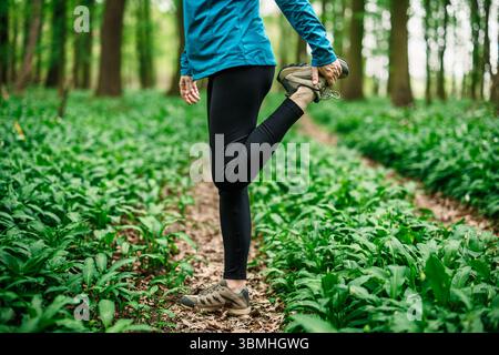 Donna che allunga la caviglia nella foresta, abbigliamento sportivo e preparazione fisica all'aperto. Preparatevi per correre Foto Stock