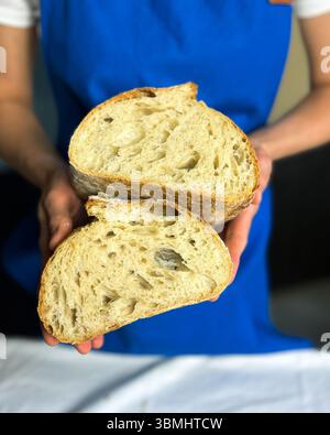 Donna che tiene in mano pane lievito madre appena sfornato preparato con antipasto senza glutine. Perfetto per blog di cottura sani, marchi di alimenti biologici e panetteria artigianale Foto Stock