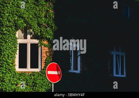 Un cartello rosso con un bordo bianco si trova sul lato di un edificio. Il cartello si trova sul lato di un edificio con l'edera che cresce sopra Foto Stock
