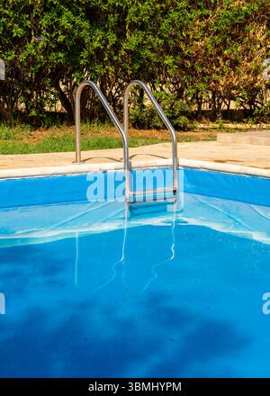 Scala metallica per piscine che conduce a calme acque turchesi. Ambiente estivo pulito e minimalista, perfetto per resort, vacanze, spa o temi di design benessere. Foto Stock