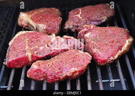 Bistecche crude condite su un barbecue Foto Stock