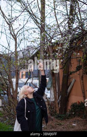 Donna carina che fa foto con lo smartphone in città primaverile all'aperto. Giovane donna che guarda i fiori primaverili e scatta foto per i social media Foto Stock