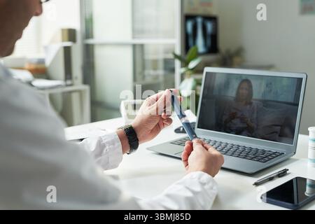 Medico di mezza età maschile caucasico che dimostra una penna per insulina durante la consultazione in telemedicina con paziente asiatica di mezza età sullo schermo del laptop in Foto Stock