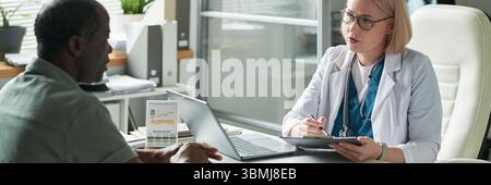 Uomo nero di mezza età consulenza medico donna caucasica di mezza età in studio medico, discutere di gestione del diabete Foto Stock