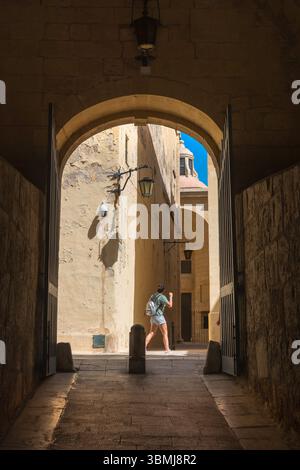 Viaggio femminile, vista di una giovane donna che indossa uno zaino che esplora da sola le strette strade della storica città fortificata di Mdina, Malta. Foto Stock