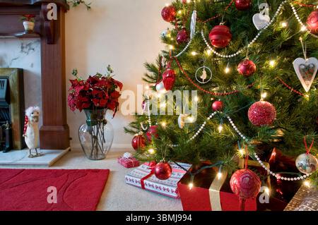 Albero di Natale parziale decorato in rosso e oro con camino e decorazioni poinsettia e ornamento di anatra natalizia Foto Stock
