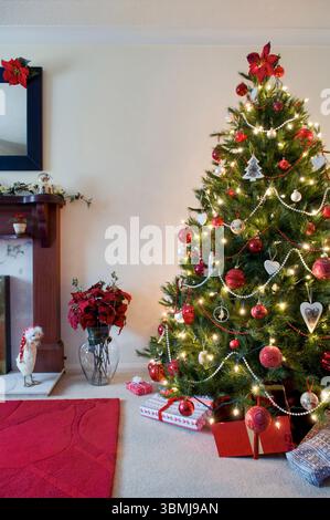 Albero di Natale decorato in rosso e oro con camino e decorazioni poinsettia Foto Stock