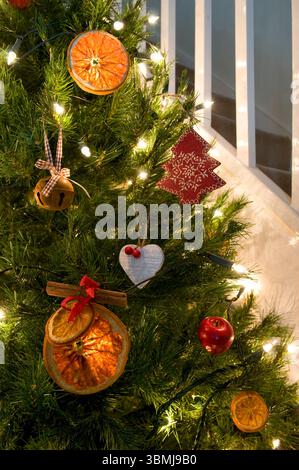 Albero di Natale decorato in un tema rustico di fette d'arancia, ornamenti in legno e mele finte, mostrando un albero di natale parziale Foto Stock
