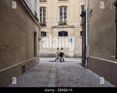 Due donne che camminano lungo una stretta strada acciottolata a parigi Foto Stock